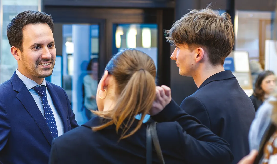 Christoph Wiederkehr spricht mit zwei jungen Teilnehmenden und lächelt während eines persönlichen Austauschs.