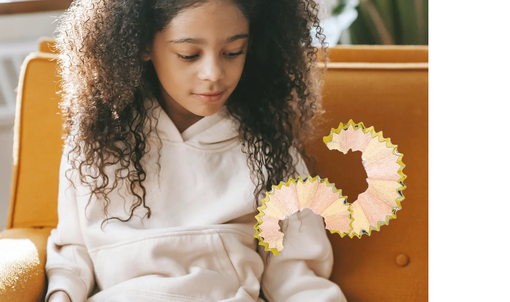 Mädchen im weißen Hoodie auf orangefarbenem Sessel, vor ihm eine spiralförmige Bleistiftspäne.