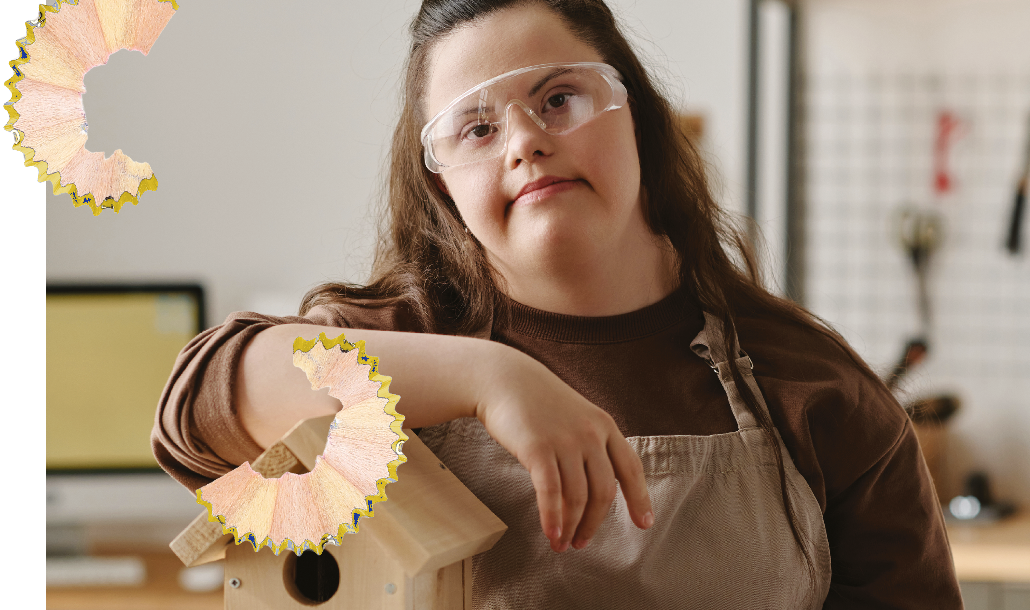 Eine junge Frau mit Schutzbrille und Schürze lehnt an einem kleinen Holzhaus und schaut in die Kamera, ergänzt durch Bleistiftspäne.